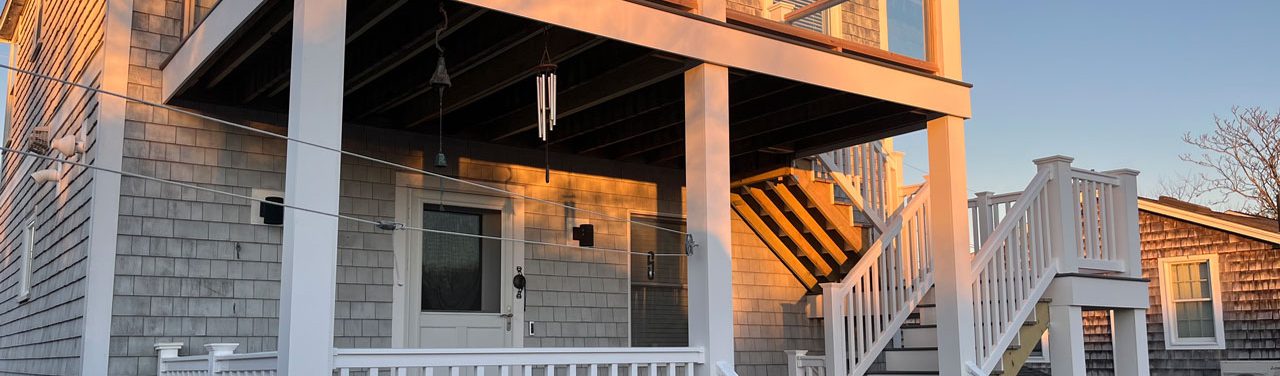 A cedar-shingled home with a covered deck and stairs