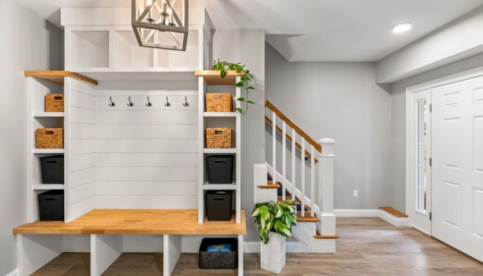 Well-organized entryway with white shiplap-backed built-in unit, natural wood bench top, black coat hooks, woven baskets on open shelves, pendant light overhead, and adjacent staircase with wood treads and white railings.